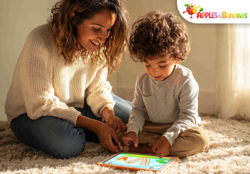 A toddler sitting on the floor with a tablet, smiling while playing an educational game. Colorful icons of animals, puzzles, and musical notes are visible on the screen, symbolizing memory, problem-solving, and language learning.