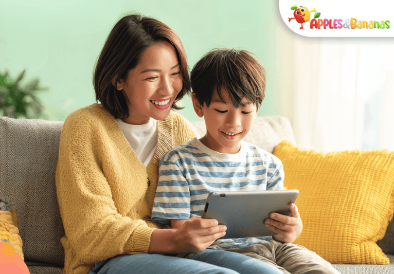 A smiling parent and child sitting together, using a tablet for learning in a bright, colorful room, symbolizing flexible digital education anytime and anywhere.