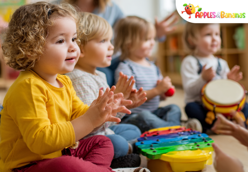 Preschool children learning through music and rhythm in a bright classroom, clapping, singing, and playing simple instruments with a teacher guiding the activity.